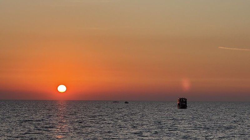 The setting sun over a huge lake in Asia, to the right there is a silhouetted boat