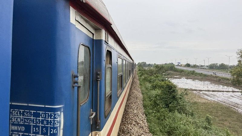 A blue train passing a rice paddy field